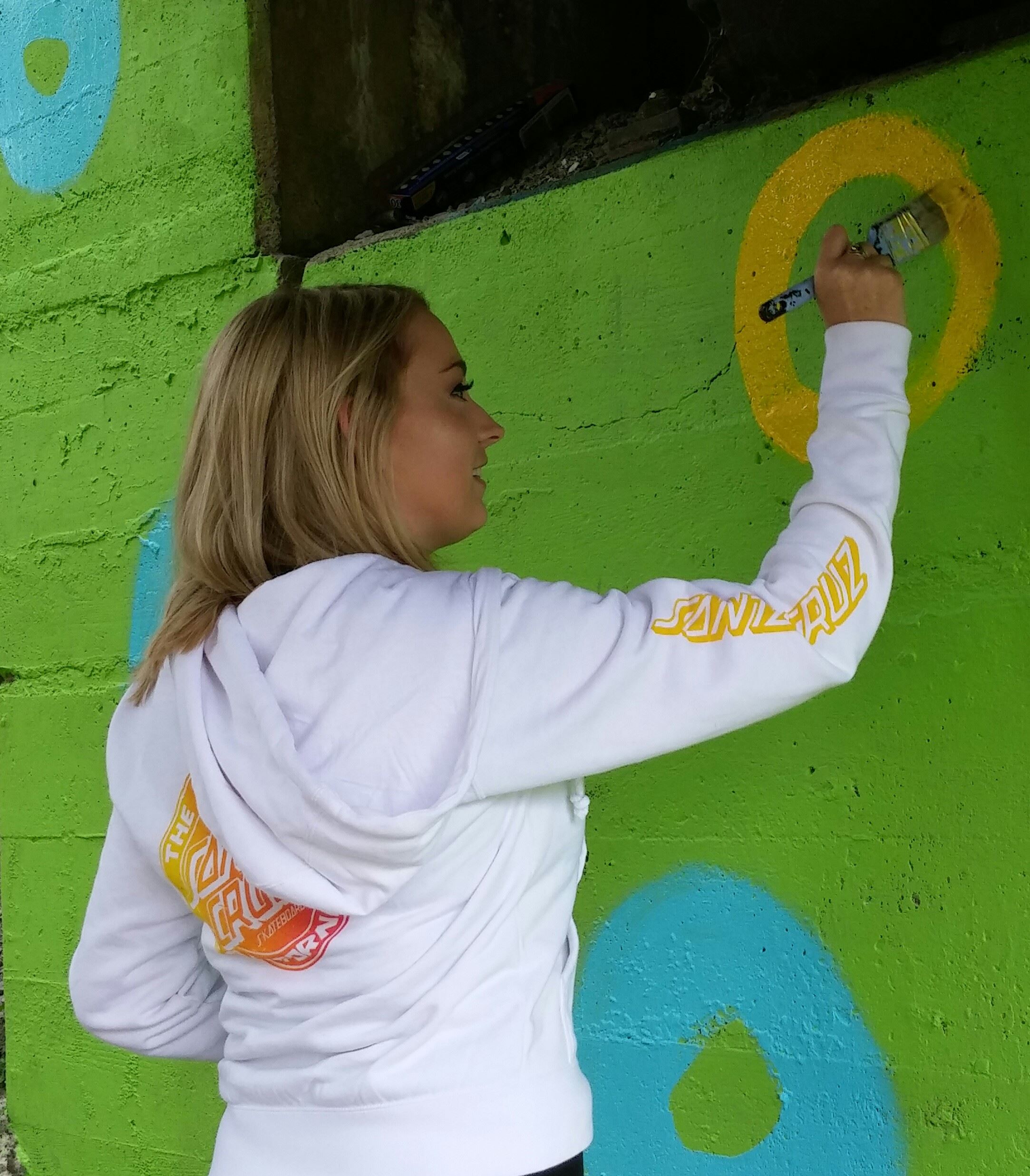 Teenager in white sweatshirt painting a yellow circle on a neon green painted wall