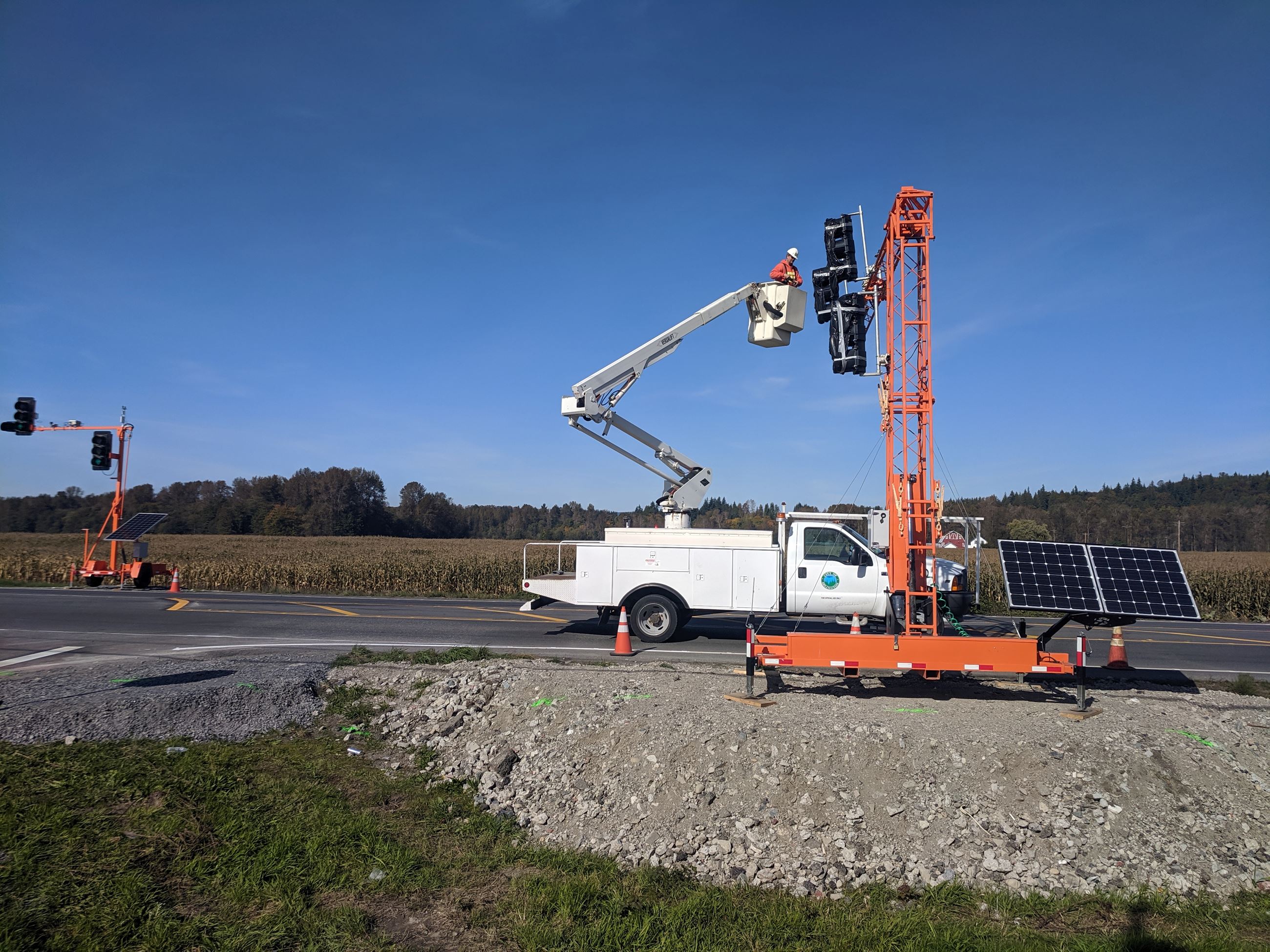 city employee in orange sweatshirt and white hardhat takes black plastic off of temporary traffic si